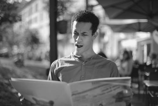 Jonge man leest verbaasd de krant op een terras