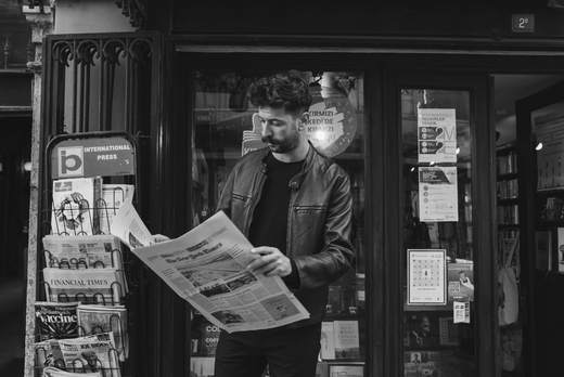 Man in leren jas leest de krant voor een kiosk