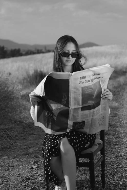 Vrouw met zonnebril leest de krant op een stoel in een veld